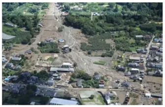 大雨による被害の空撮写真。川が氾濫し、周囲の住宅や農地が泥や土砂で埋まり、広範囲にわたって被害を受けている様子が確認できる。
