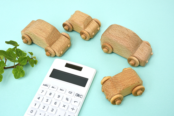 水色の背景に置かれた電卓と木製の車のおもちゃの画像