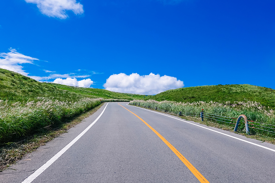 青空の下、緑の丘の間を抜ける舗装された道路の画像